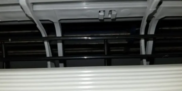 Vue rapprochée de l'intérieur d'un climatiseur, montrant des composants en plastique blanc, une calandre noire et un intérieur sombre.