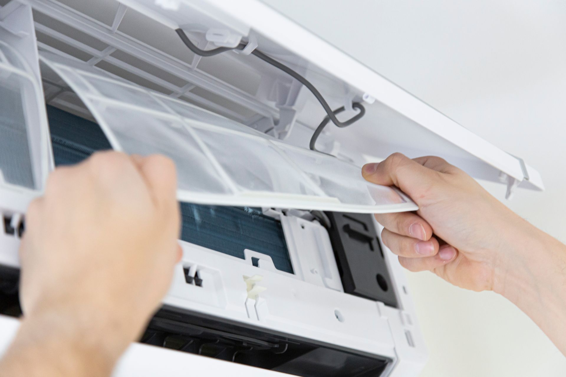 Mains retirant un filtre à air d'un climatiseur blanc.