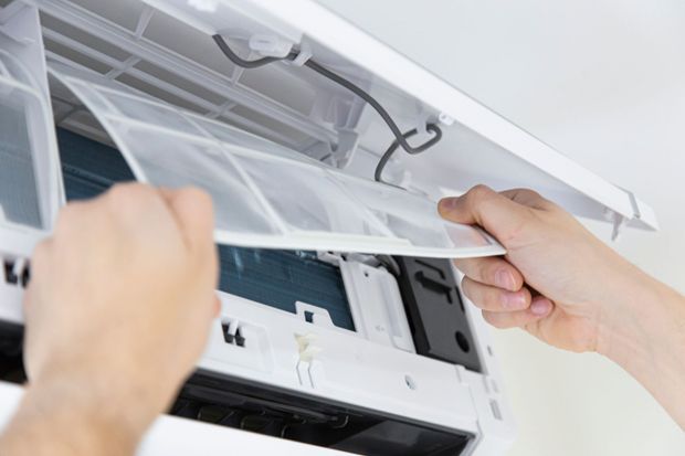 Mains retirant un filtre à air d'un climatiseur blanc.