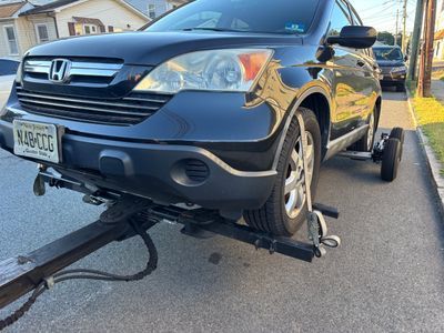 Black Honda CRV being towed on a tow dolly on a paved street.