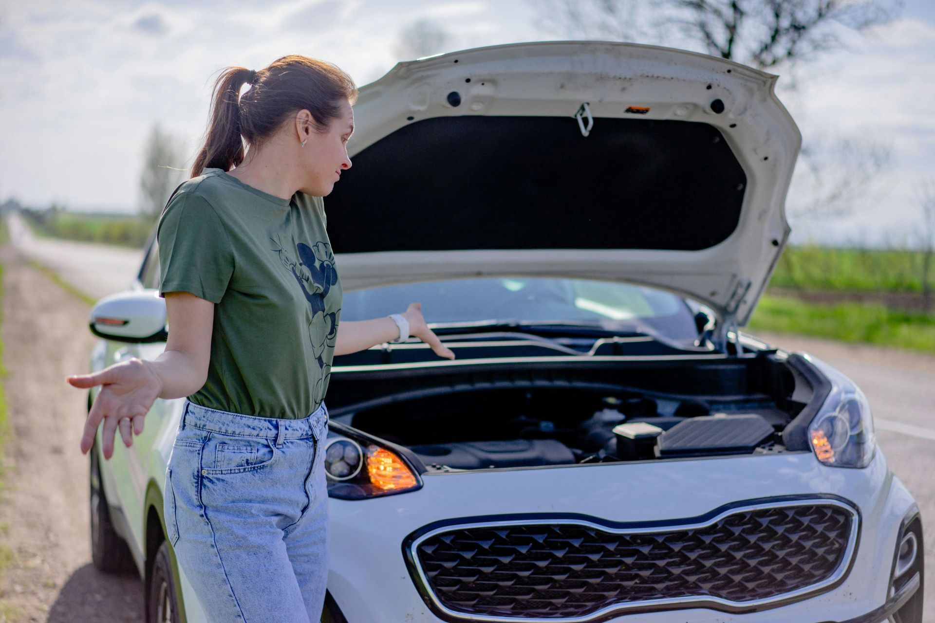 Woman with open car hood on a roadside, looking frustrated.