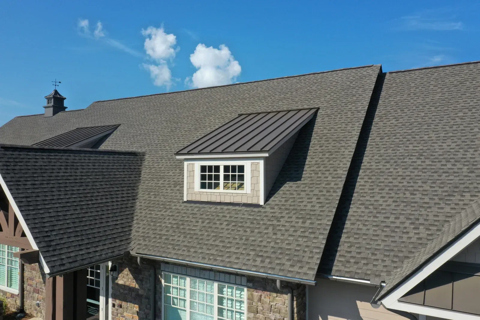 A house with gray shingle roofs, dormer window, and blue sky.