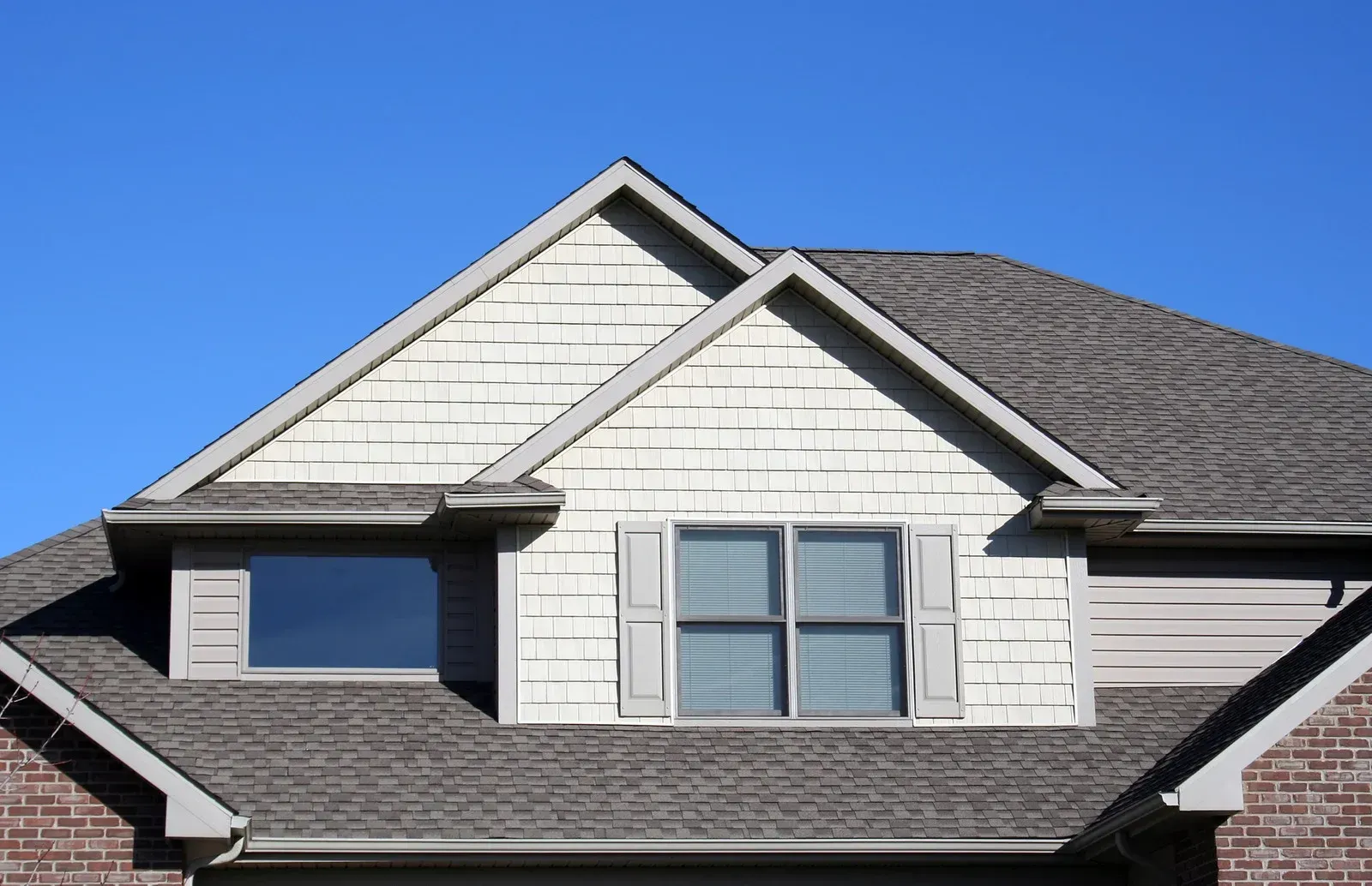 The roof of a house with two windows and a gray roof.