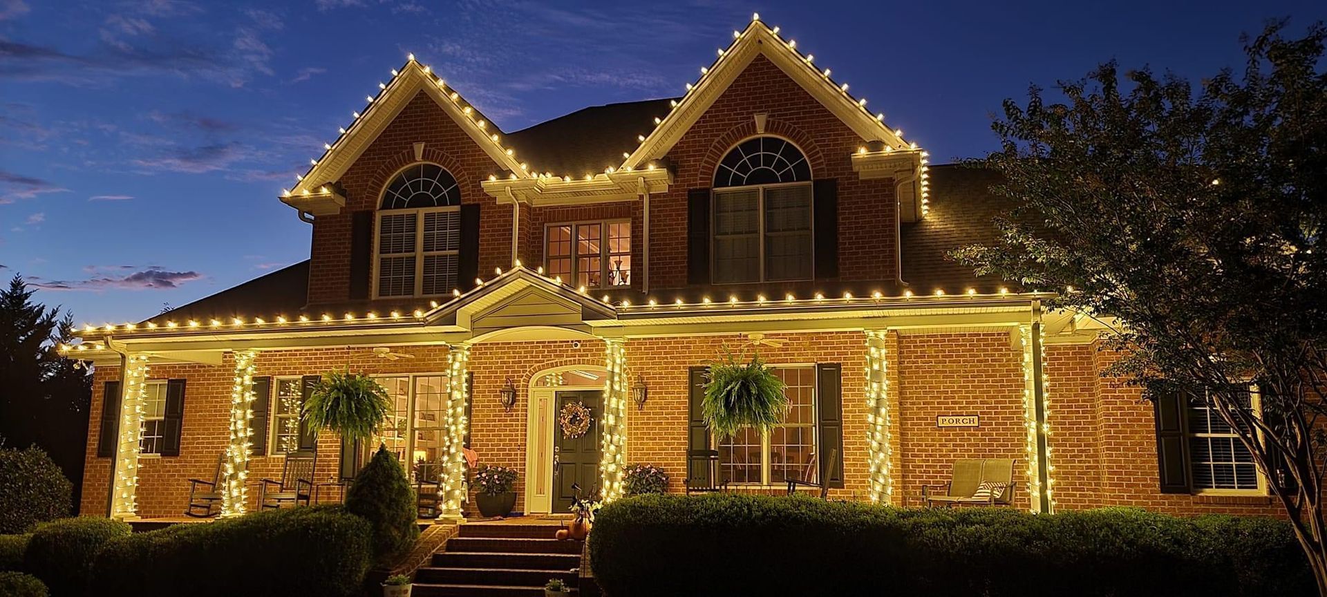 House covered in Christmas lights; red, green, and blue lights on trees and shrubs in snowy setting at night.