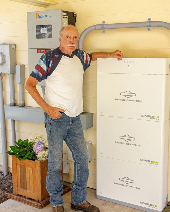 Man standing beside a large white appliance in a utility room, hand resting on top, with electrical panels behind him.