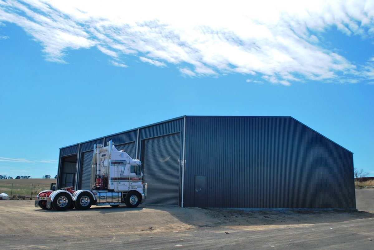 Semi-truck parked next to a large, dark metal shed under a blue sky— Northern Rivers Sheds in South Lismore, NSW