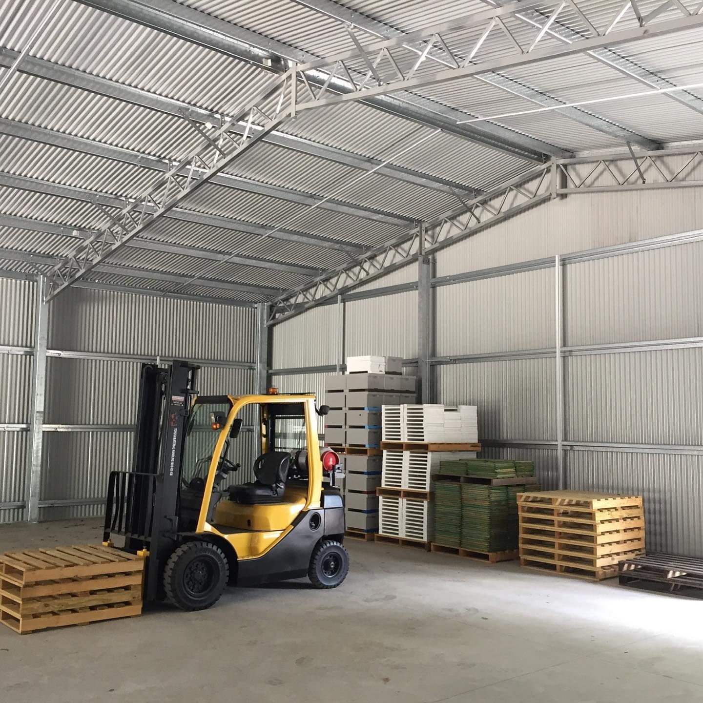 Yellow forklift in a metal warehouse with pallets stacked against the wall.-Northern Rivers Sheds in South Lismore, NSW