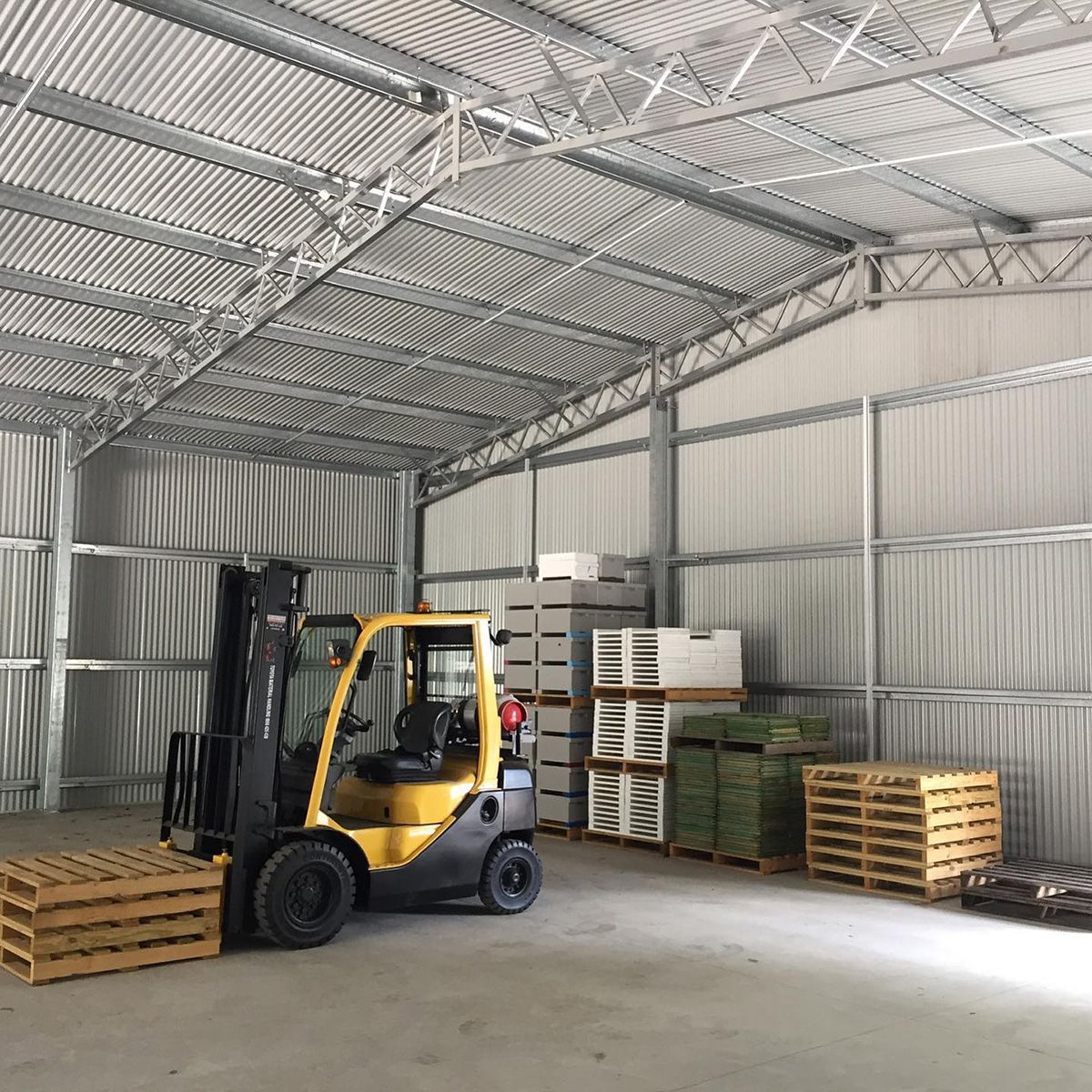 Inside a metal warehouse, a yellow forklift and stacked pallets— Northern Rivers Sheds in Byron Bay, NSW