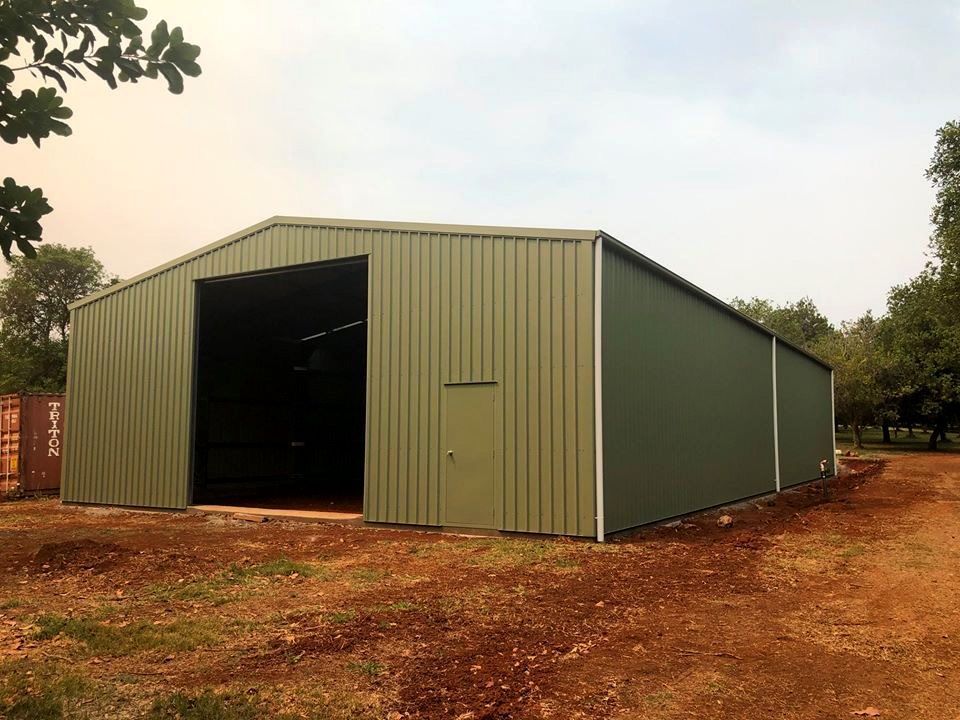 Green metal shed with large open entrance and small side door, set in a dirt field— Northern Rivers Sheds in Byron Bay, NSW