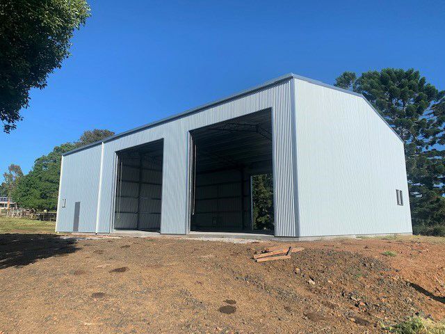 White metal shed with two large open bays on a grassy hillside under a clear blue sky— Northern Rivers Sheds in Byron Bay, NSW