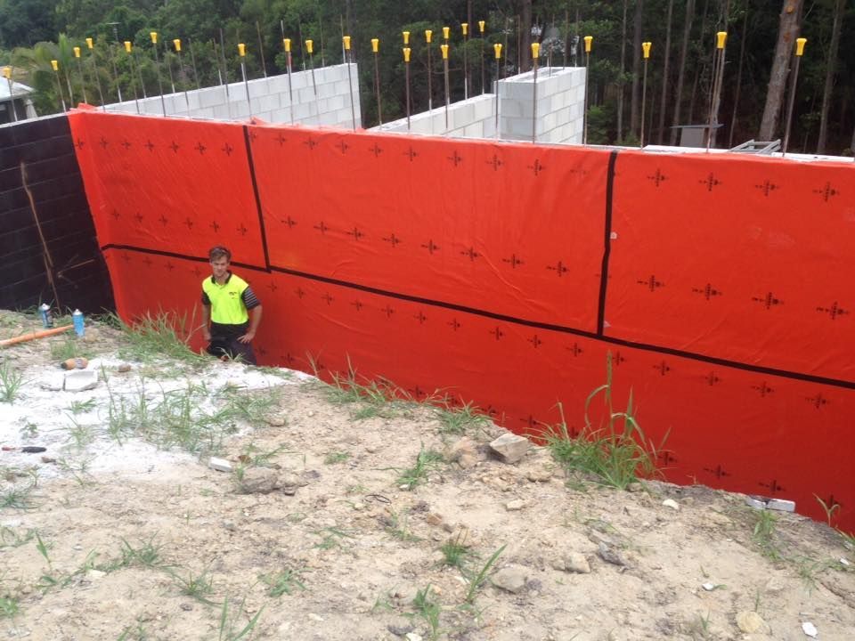 Man Standing by a Bright Orange Wall Possibly Foundation Waterproofing With Black Seams — All Pest QLD In Buderim, QLD