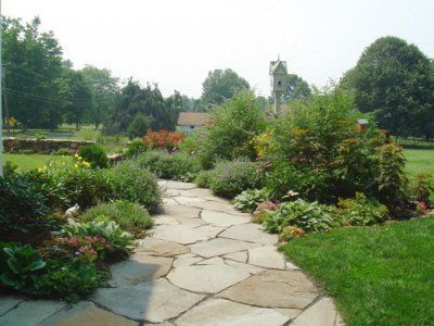 A stone walkway in a garden with a clock tower in the background