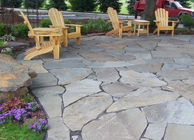 A group of wooden chairs are sitting on a stone patio.