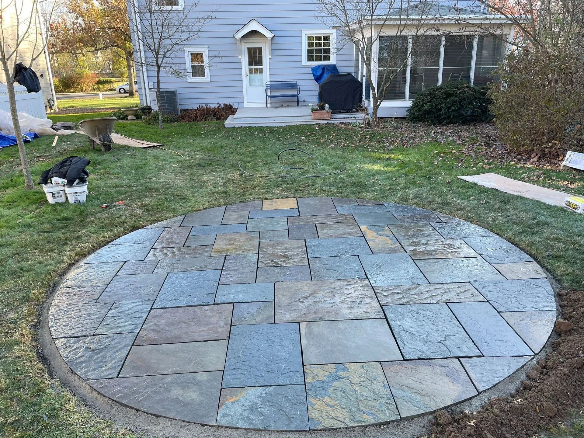 A circular stone patio in a backyard in front of a house.