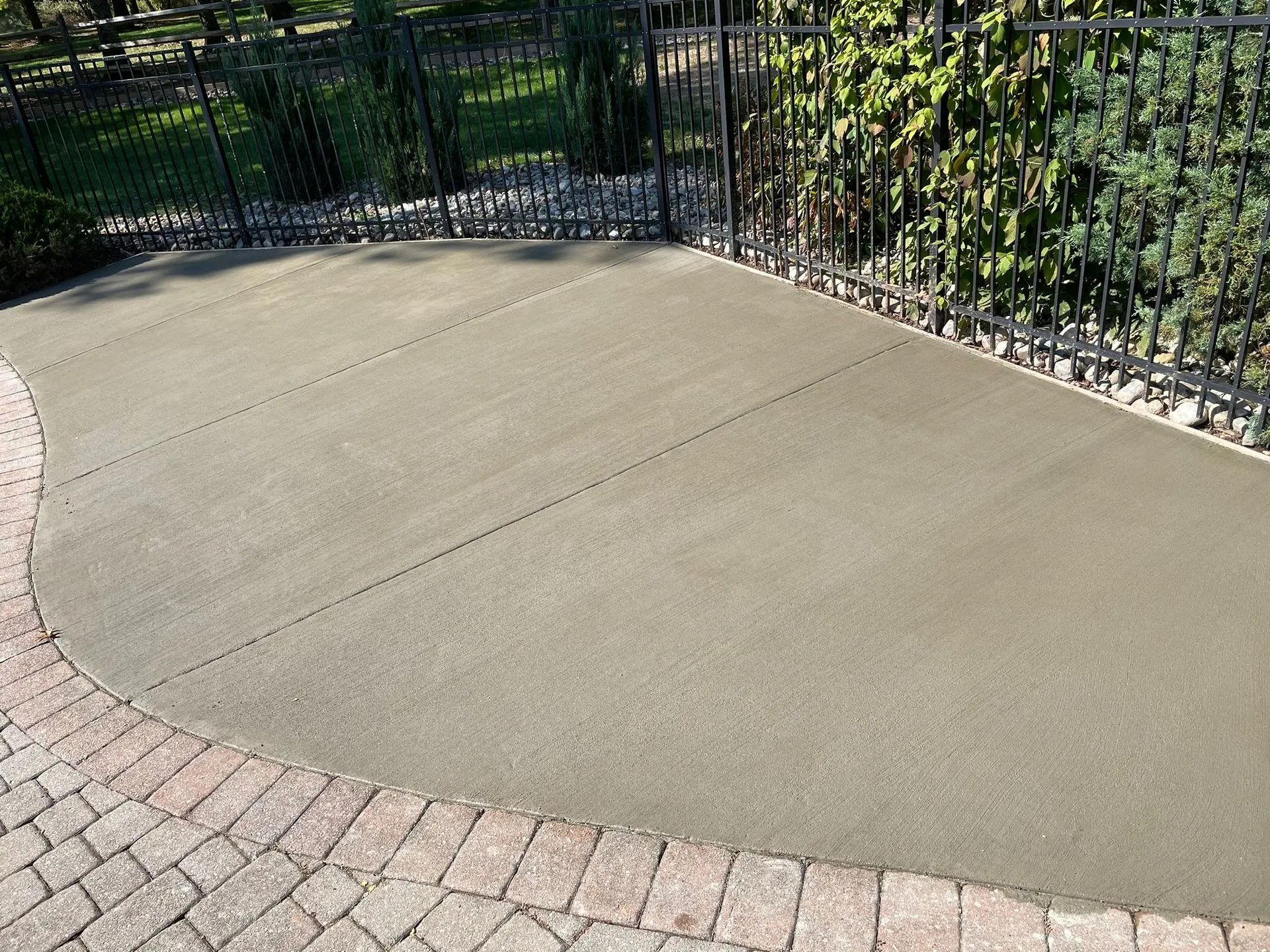 A concrete driveway surrounded by bricks and a metal fence