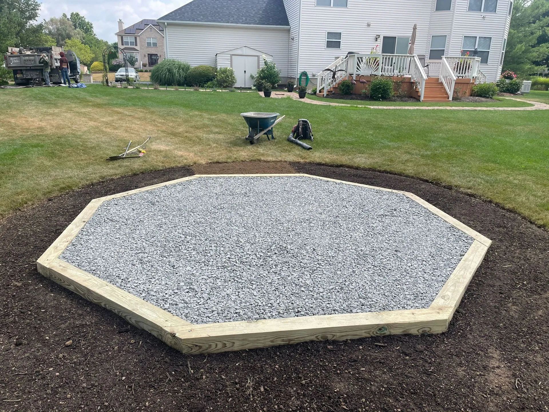 A wheelbarrow is sitting in the middle of a gravel area in front of a house.