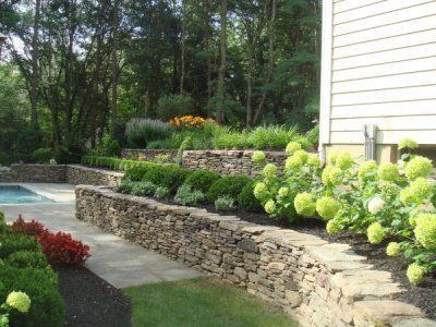 A stone wall surrounds a swimming pool in a backyard.