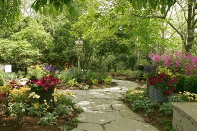 A stone walkway surrounded by flowers and trees in a garden.