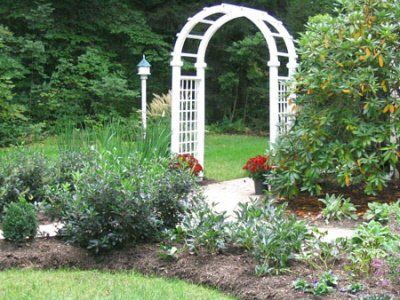 A white arch is in the middle of a garden