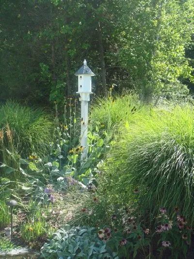 A birdhouse is sitting on top of a white pole in the middle of a garden.