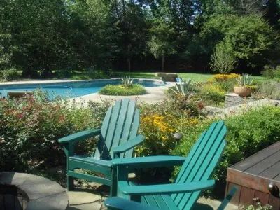 Two green adirondack chairs sit in front of a swimming pool