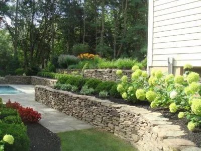 A stone wall surrounds a swimming pool in a backyard