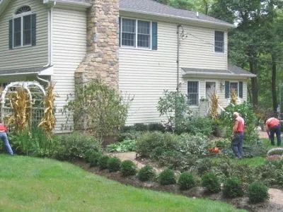 A group of people are working in a garden in front of a house.