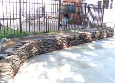 A stone wall is being built in front of a fence.