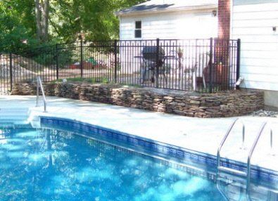 A large swimming pool surrounded by a fence and a stone wall.