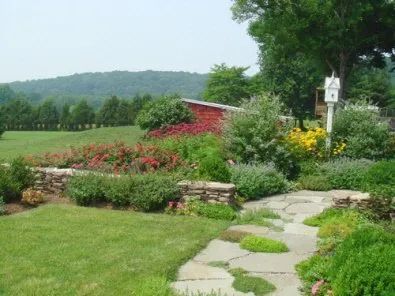 A stone walkway in a garden with a red barn in the background