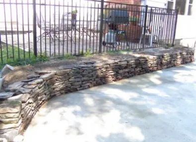 A stone wall is being built in front of a fence.
