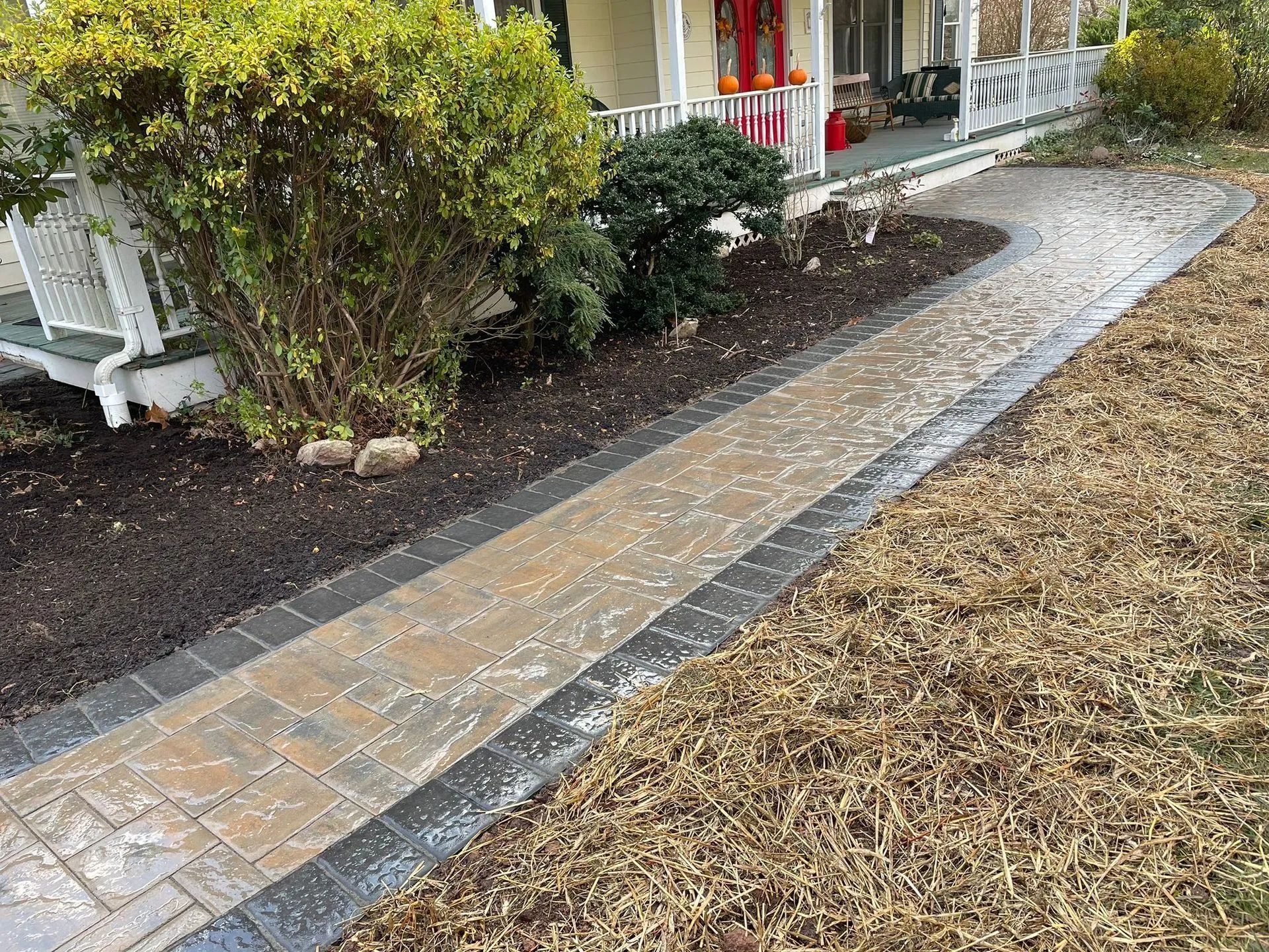 A brick walkway leading to a house with a porch.