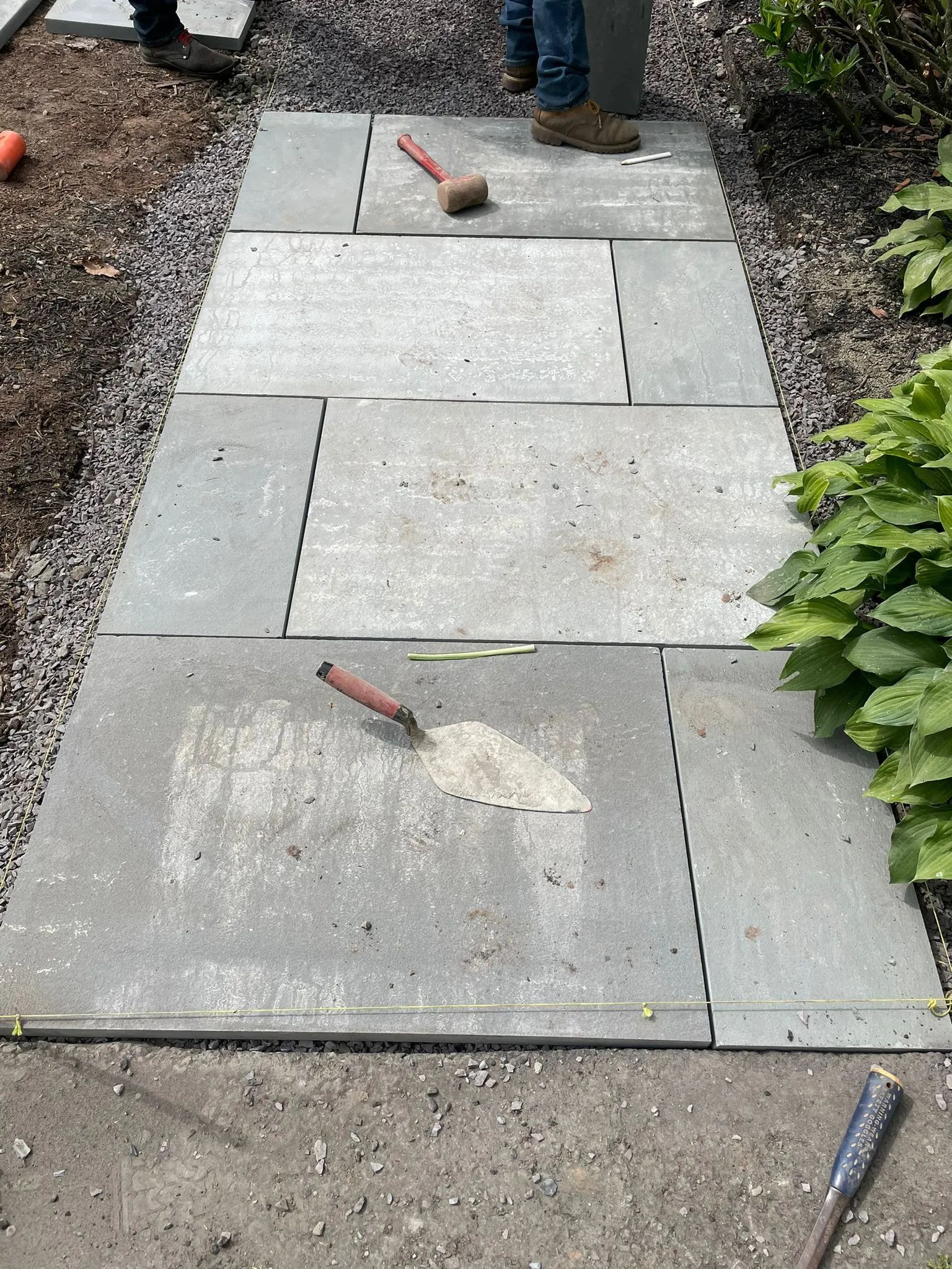 A person is standing on a sidewalk with a shovel and a hammer.