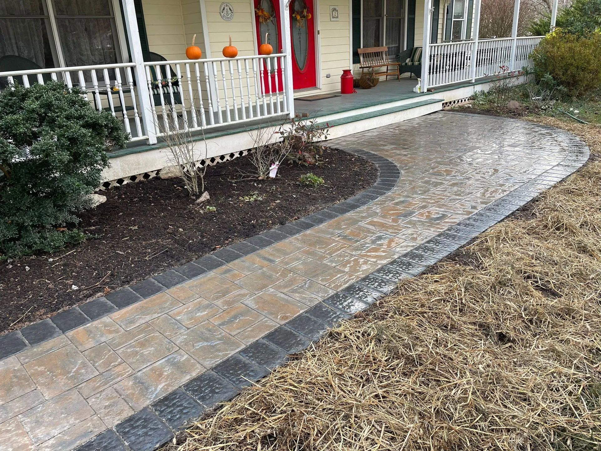A brick walkway leading to a house with pumpkins on the porch.