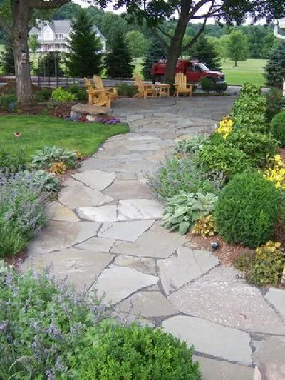 A stone walkway leading to a lawn with chairs in the background.