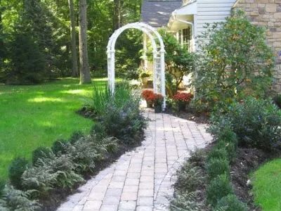 A brick walkway leading to a house with a white archway