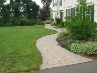 A brick walkway leading to a house with a lush green lawn
