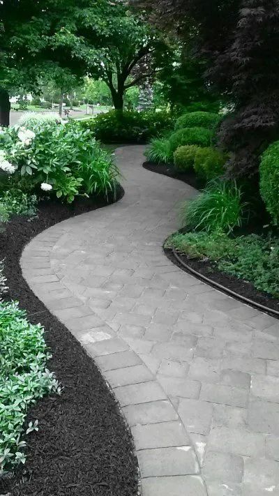A curved walkway in a garden surrounded by trees and bushes.