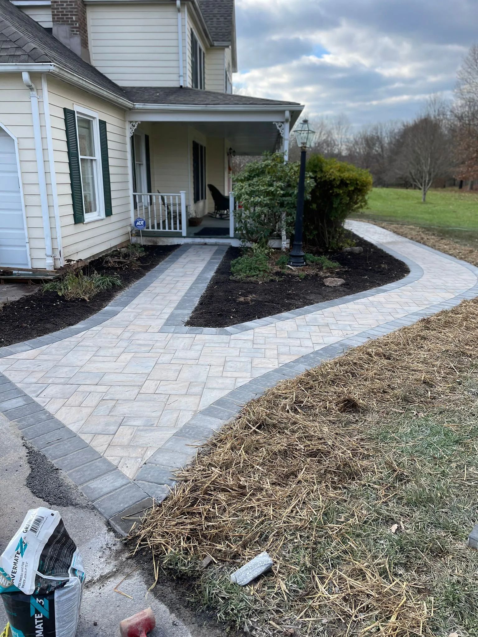 A brick walkway leading to a house with a porch.