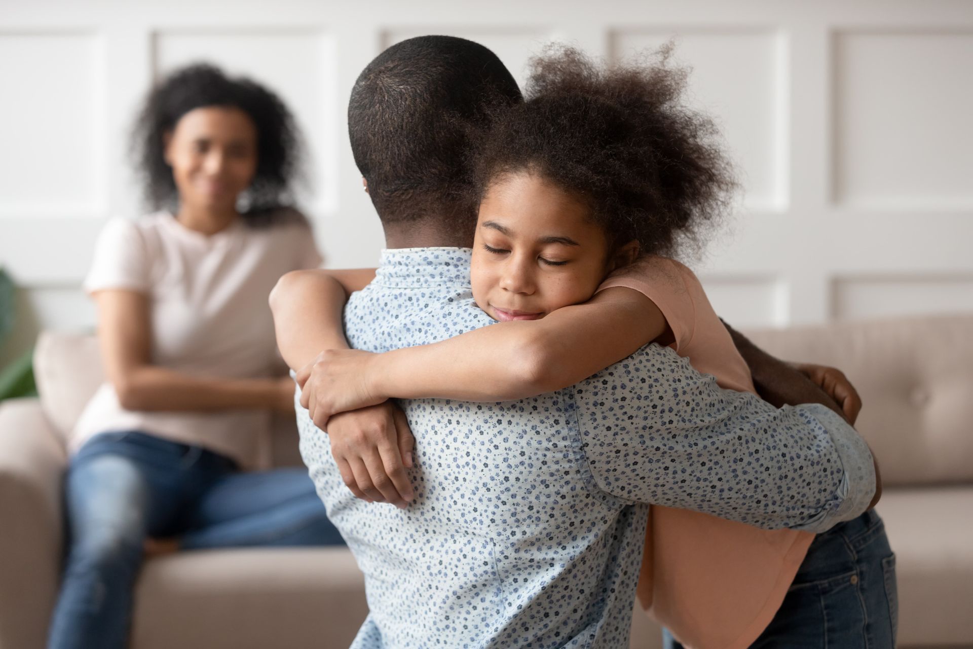 Two people embrace on a couch while a seated woman watches in the background.