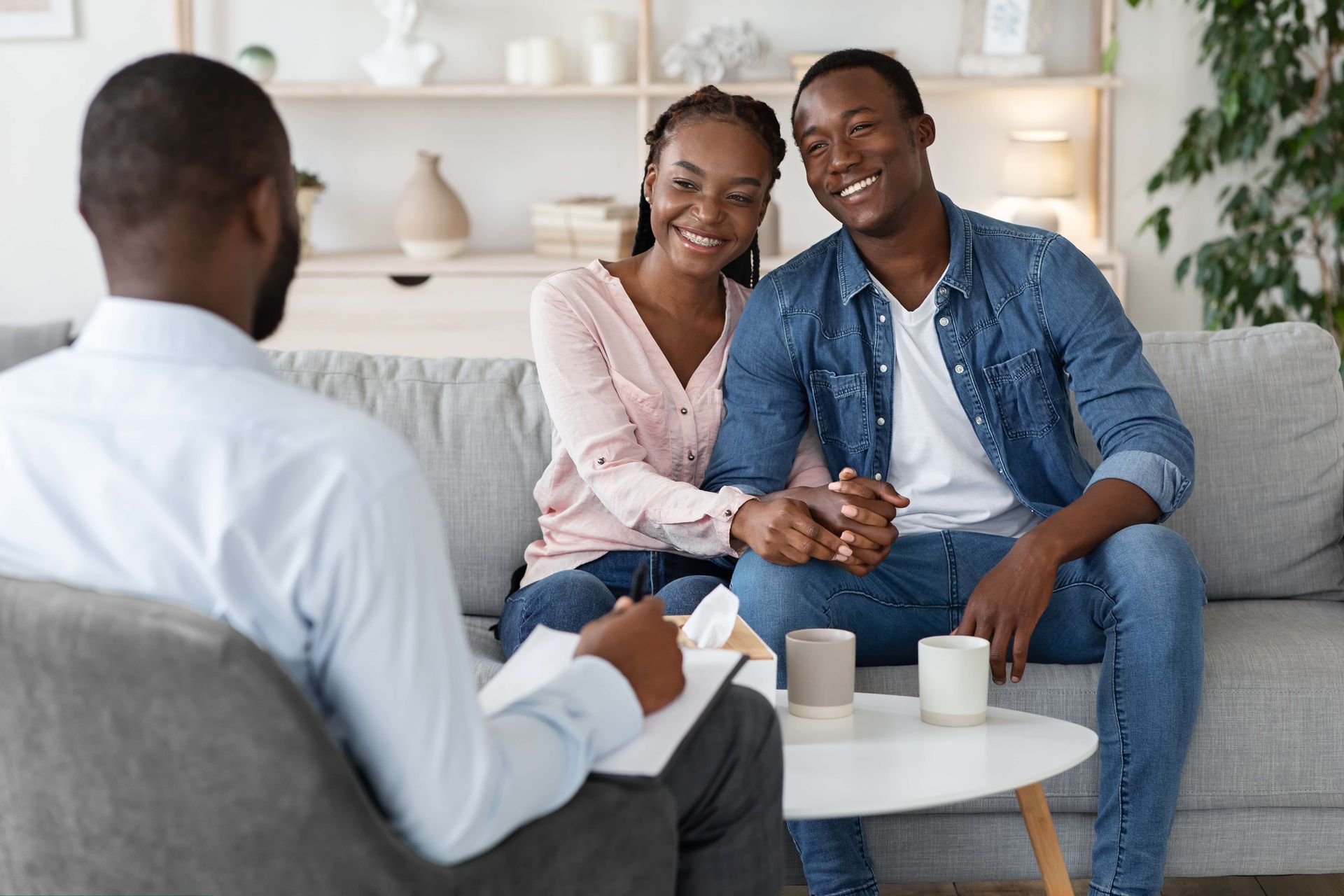 Couple smiling on a sofa during a counseling session, with a therapist seated across from them.