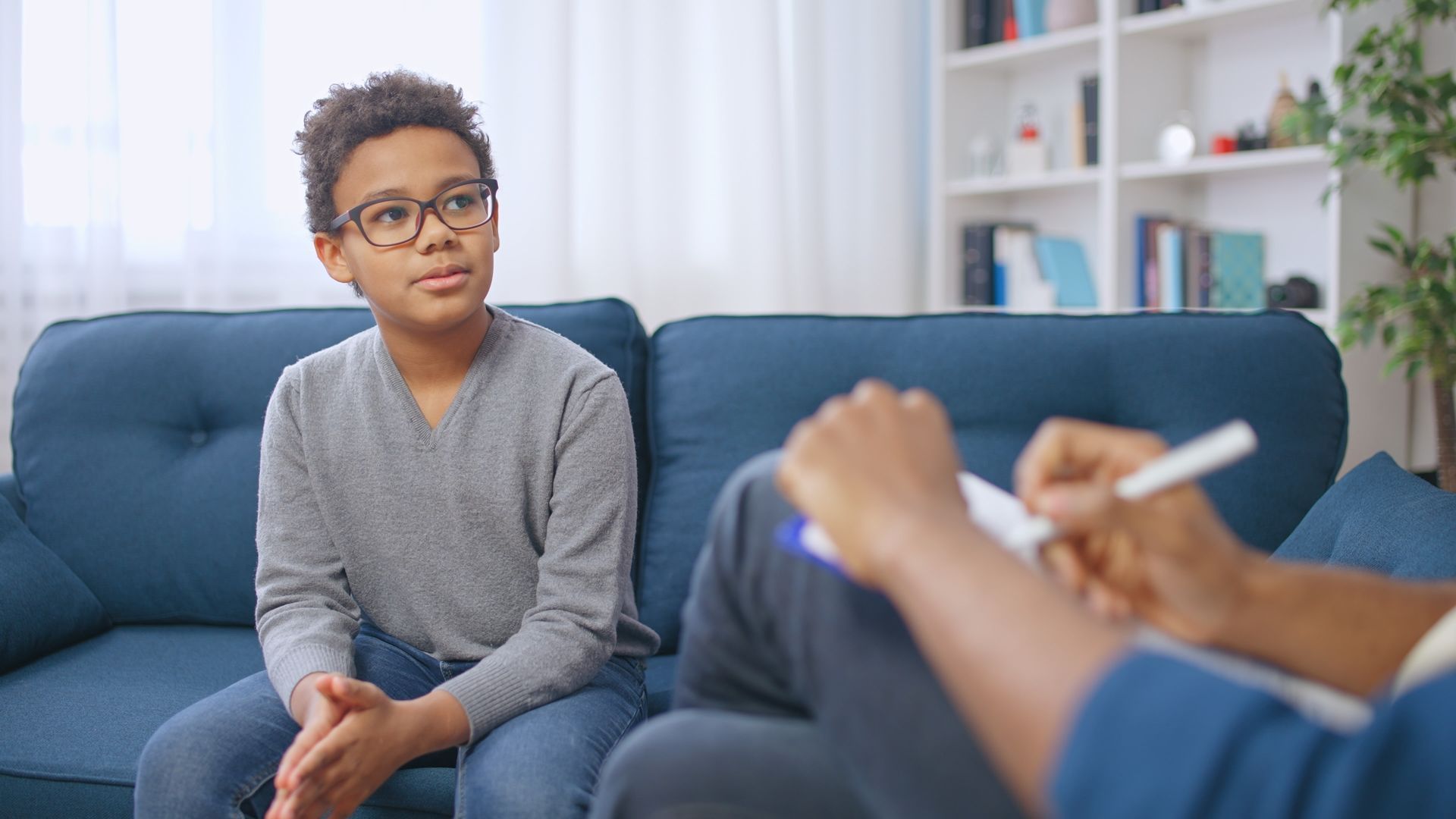 Boy sitting on a couch, listening to a person taking notes during a conversation.