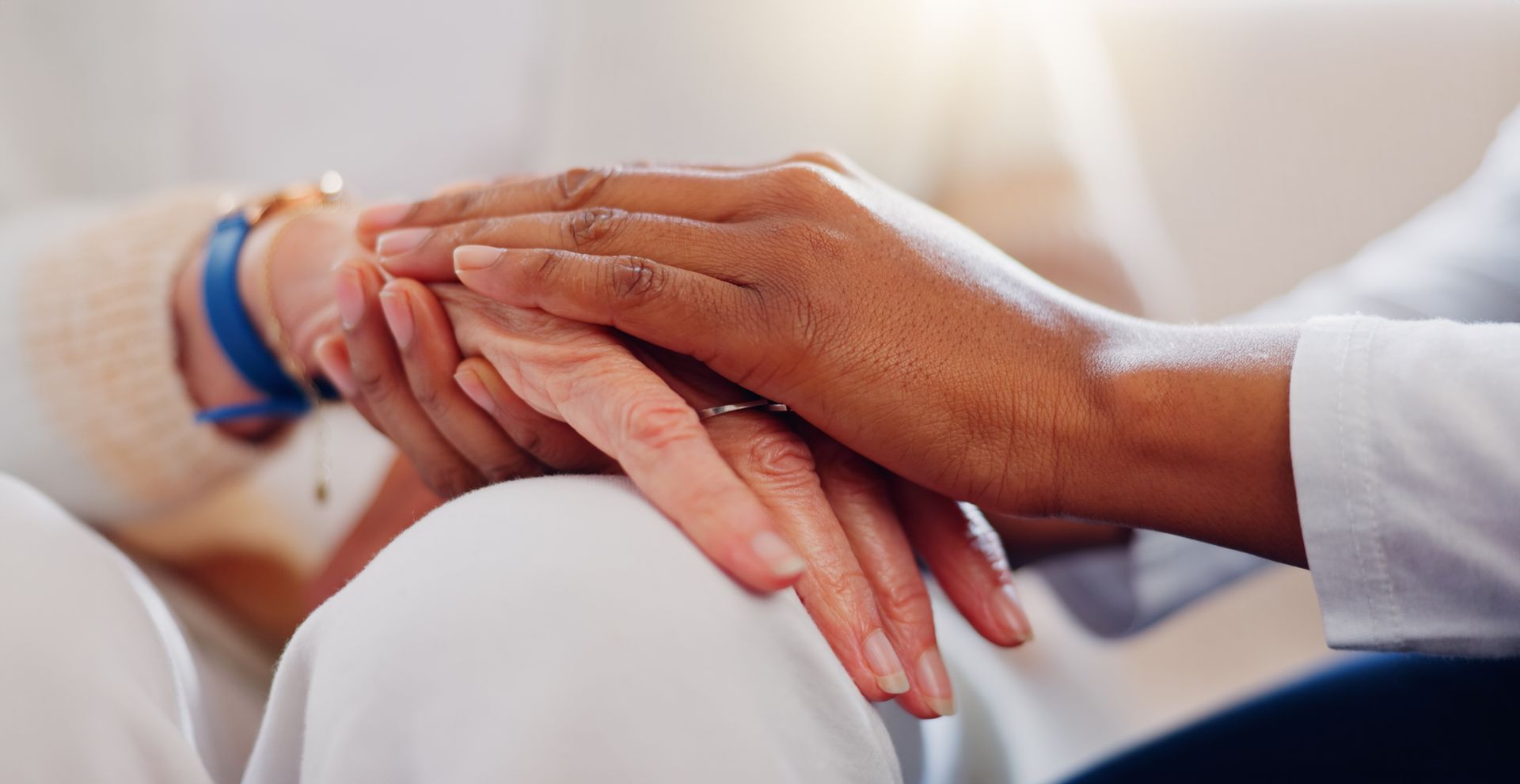 Hands gently clasped together in a comforting gesture on a white blanket.