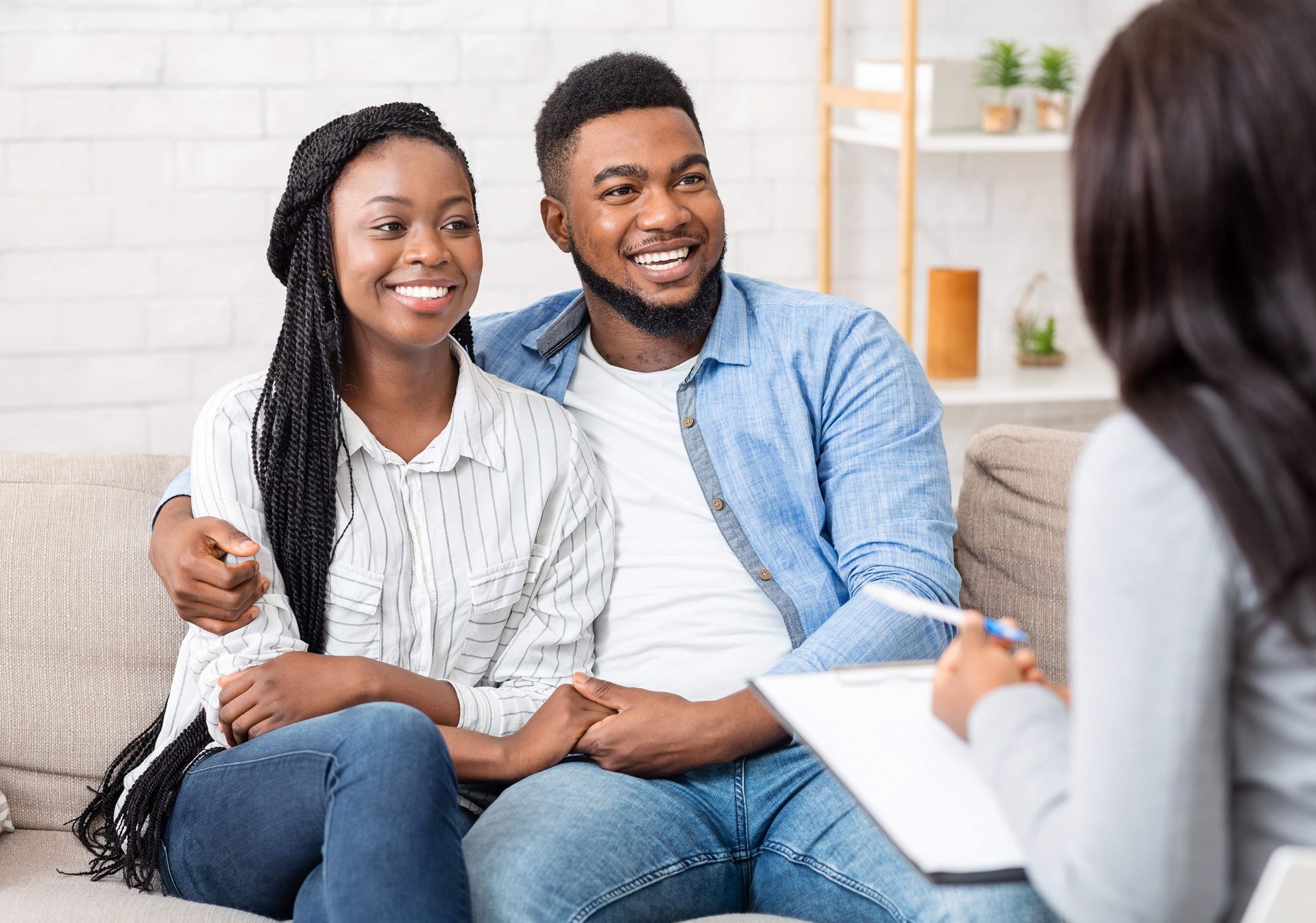 Smiling couple on a couch talking with a counselor in a bright living room.