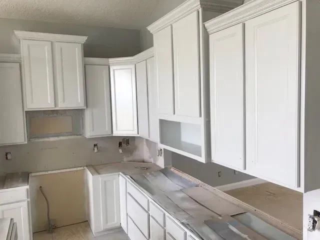 White kitchen cabinets installed above and below a countertop in an unfinished kitchen.