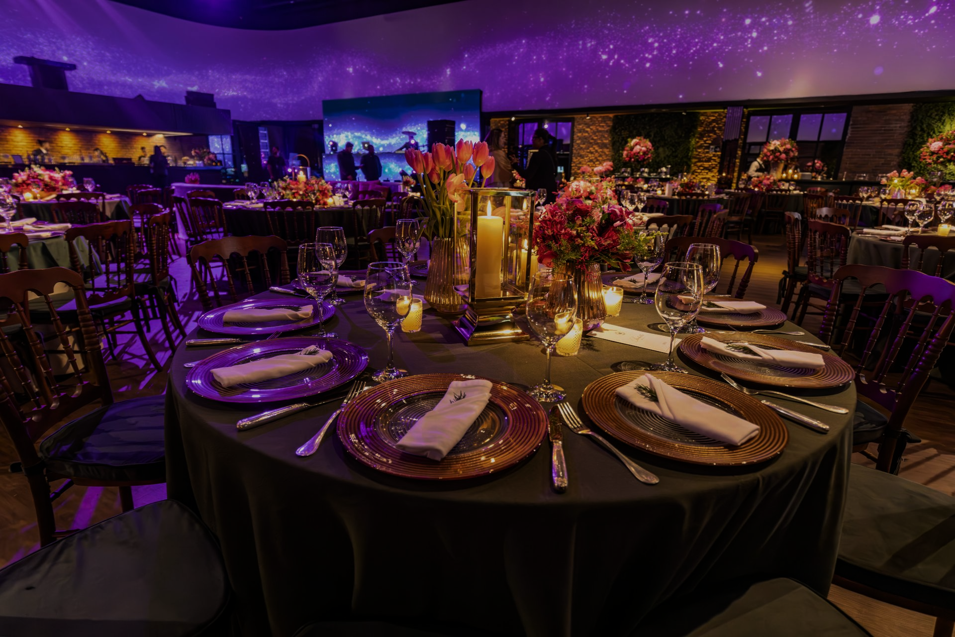 Formal dining room with tables set for a celebration. Purple and gold decor, lit by candles and overhead lights.