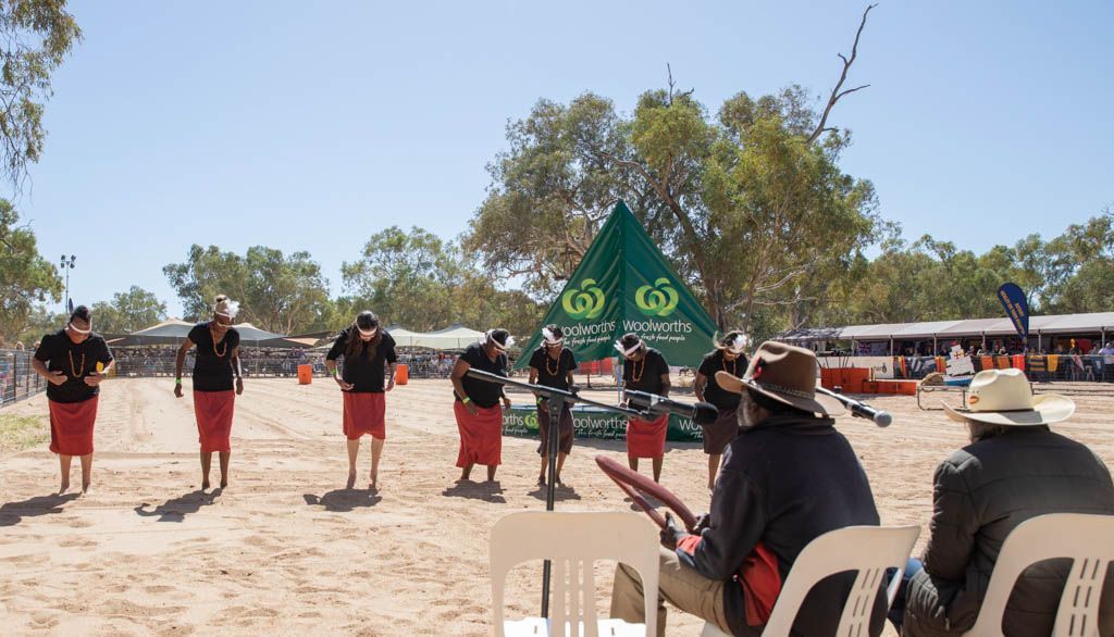 A group of people are standing in the sand playing drums.