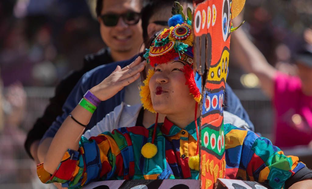 A woman in a colorful costume is holding a totem pole.