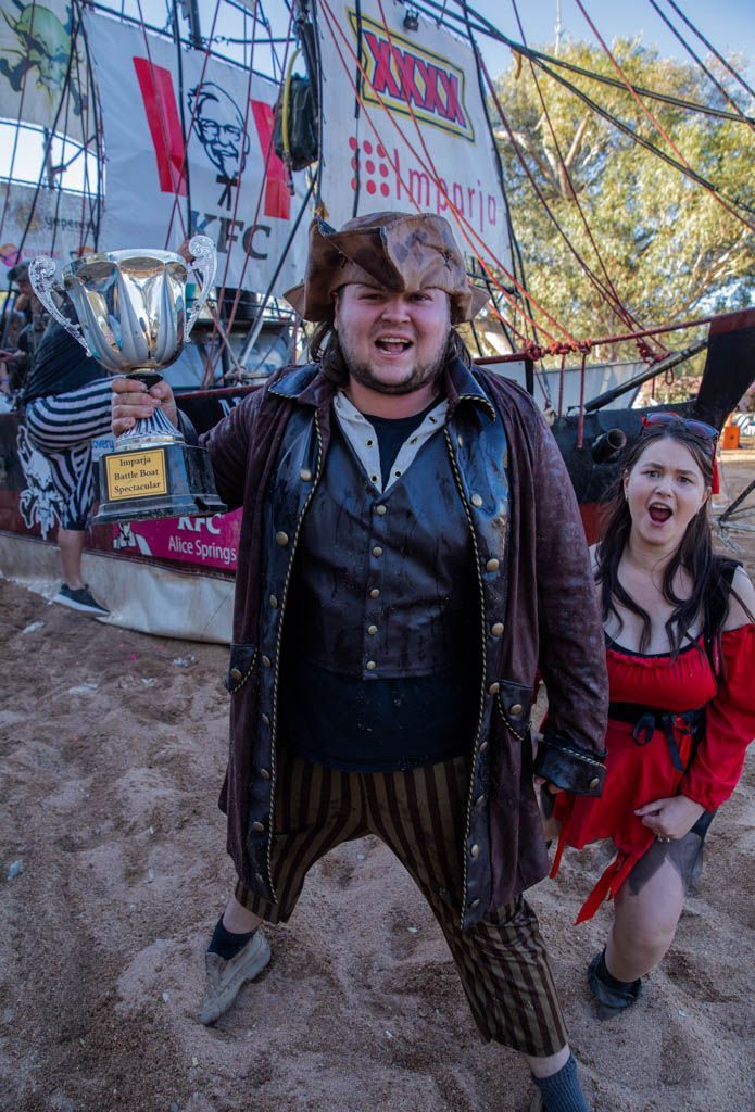 A man in a pirate costume is holding a trophy next to a woman in a red dress.