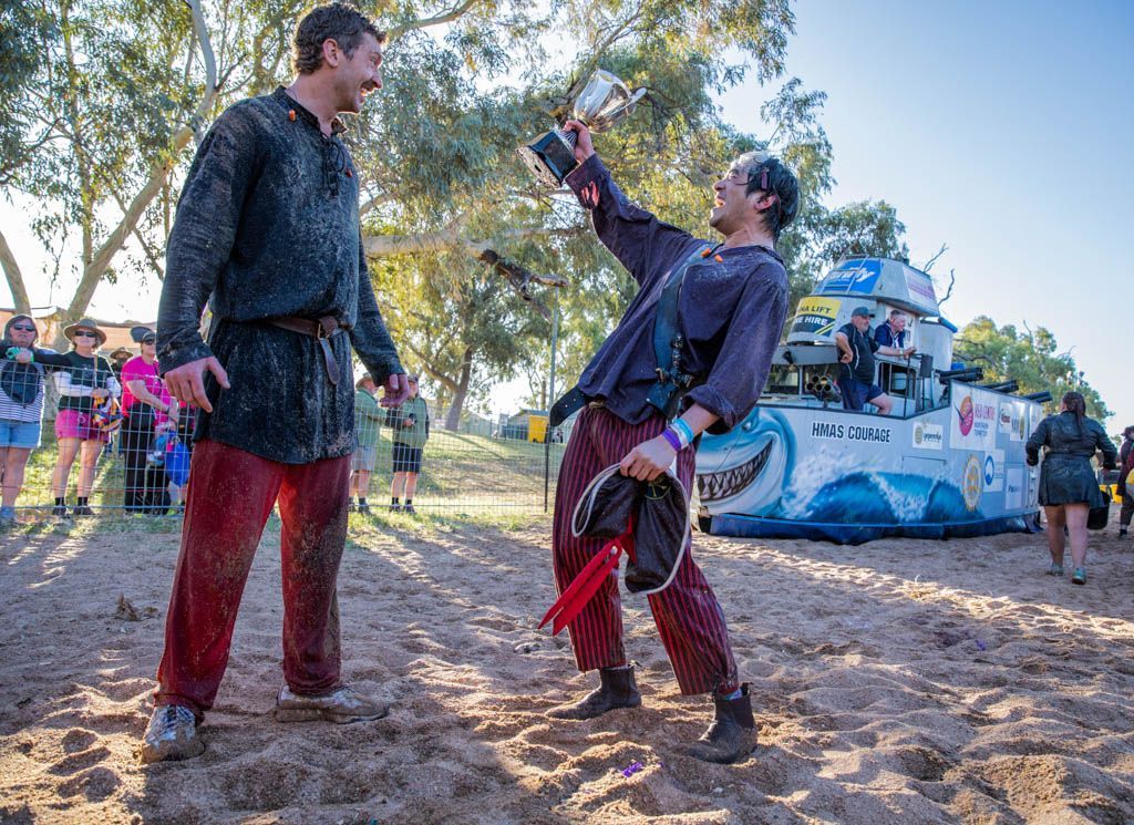 Two men are standing next to each other in the dirt.